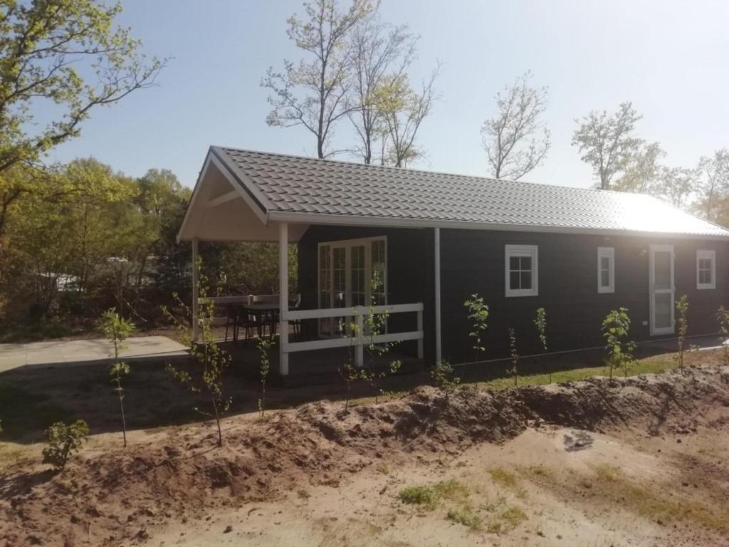 a small black house with a porch at Comfortable forest lodge with open space in Balkbrug