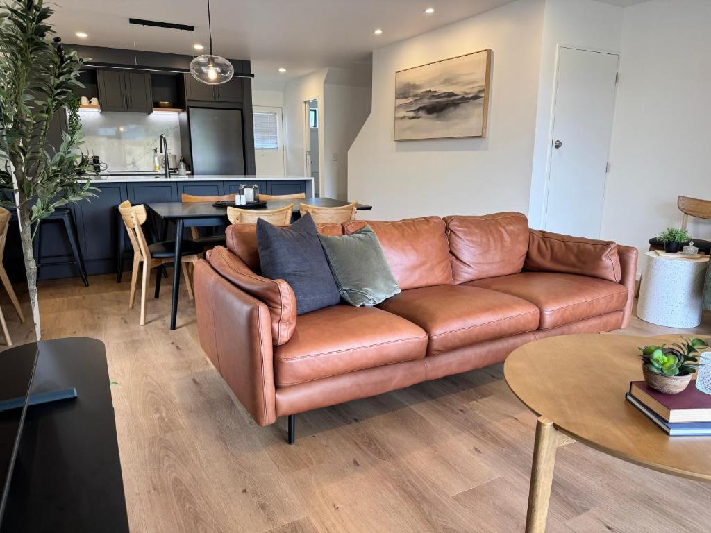 a living room with a brown leather couch and a kitchen at The Kings Domain, DUCHESS - Luxurious townhouse in the CBD! in Blenheim