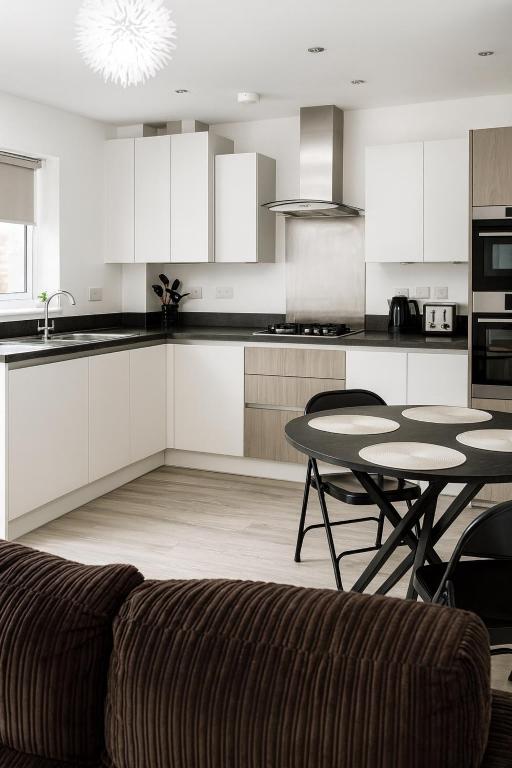 a kitchen with white cabinets and a table and a couch at Ebbsfleet Luxe in Swanscombe