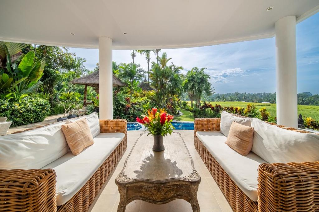 un patio avec des canapés blancs et une table avec des fleurs dessus dans l'établissement Villa Tau, à Tegalalang