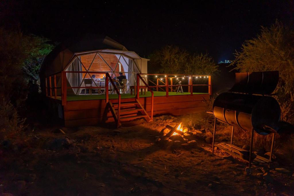 una pequeña cabaña con una chimenea encendida delante por la noche en GLAMPING CACHI EL PARAISO DE NALA, en Cachí