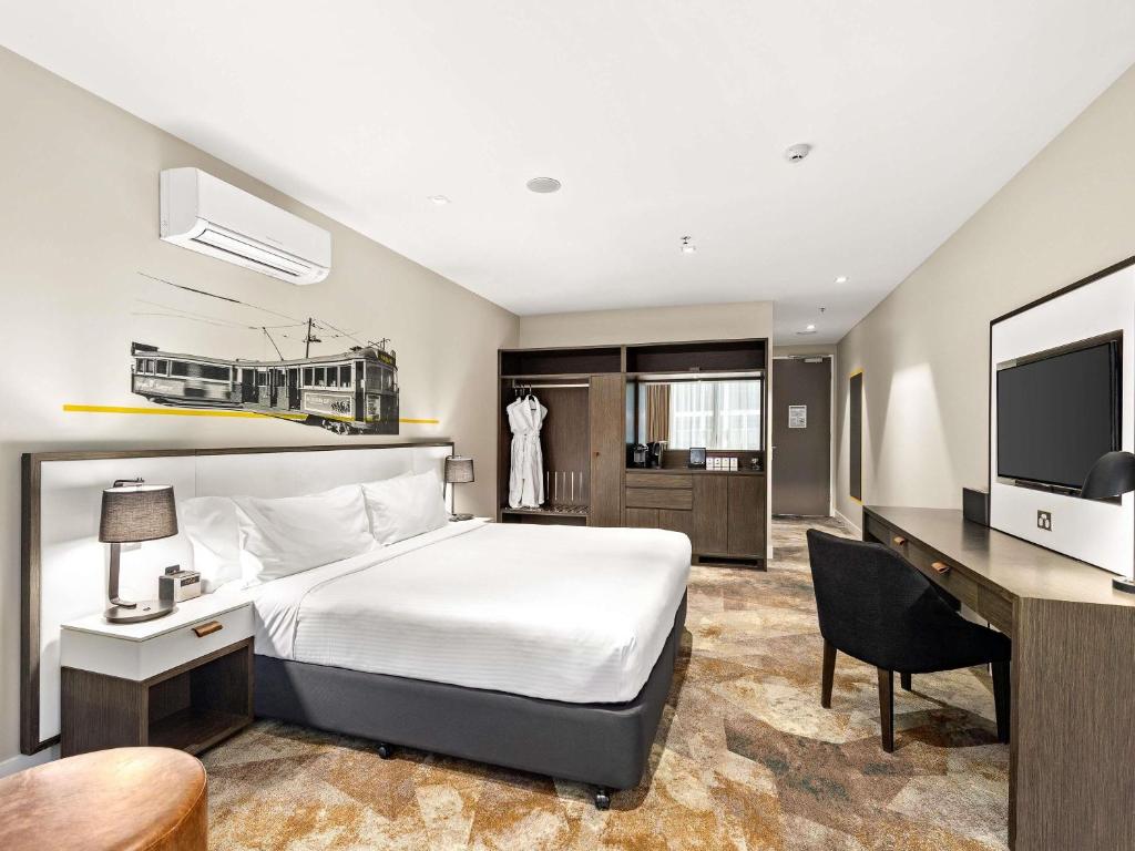 Un dormitorio con una cama, un escritorio y un televisor. en Peppers Docklands, en Melbourne