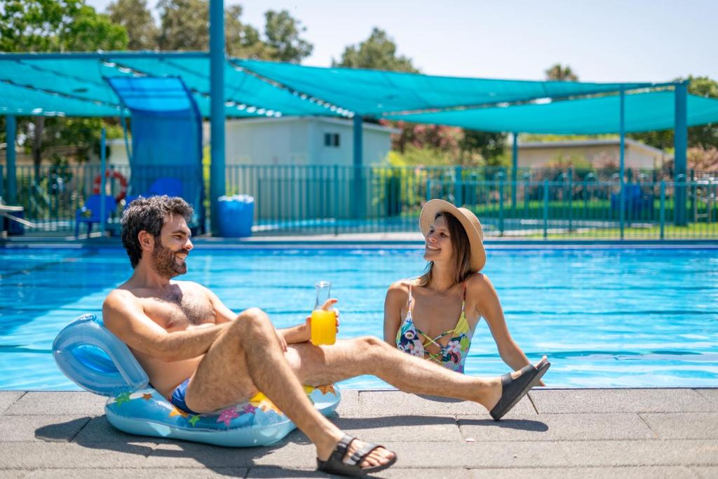 a man and woman sitting on inflatables by a pool at Etnachta Kibbutz Afik in Afik