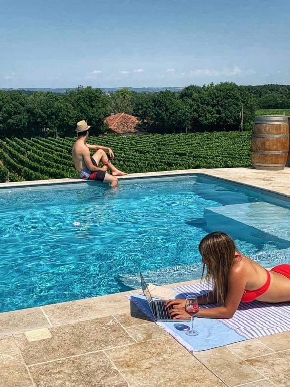 una donna sdraiata su un asciugamano con un computer portatile in una piscina di domaine de codeval a Fronton