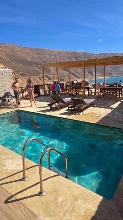 a swimming pool with blue water and picnic tables at Aloha Imsouane vue sur mer in Imsouane