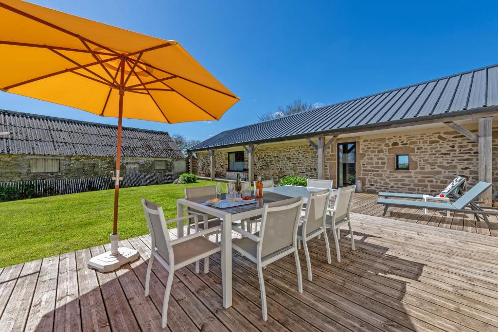 una mesa y sillas con una sombrilla en la cubierta en Gîte avec piscine privée chauffée, en Kernilis