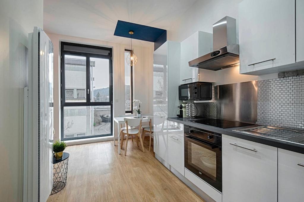 une cuisine avec des placards blancs et une grande fenêtre dans l'établissement Proche Gare, parking couvert, Wifi, à Bourgoin-Jallieu