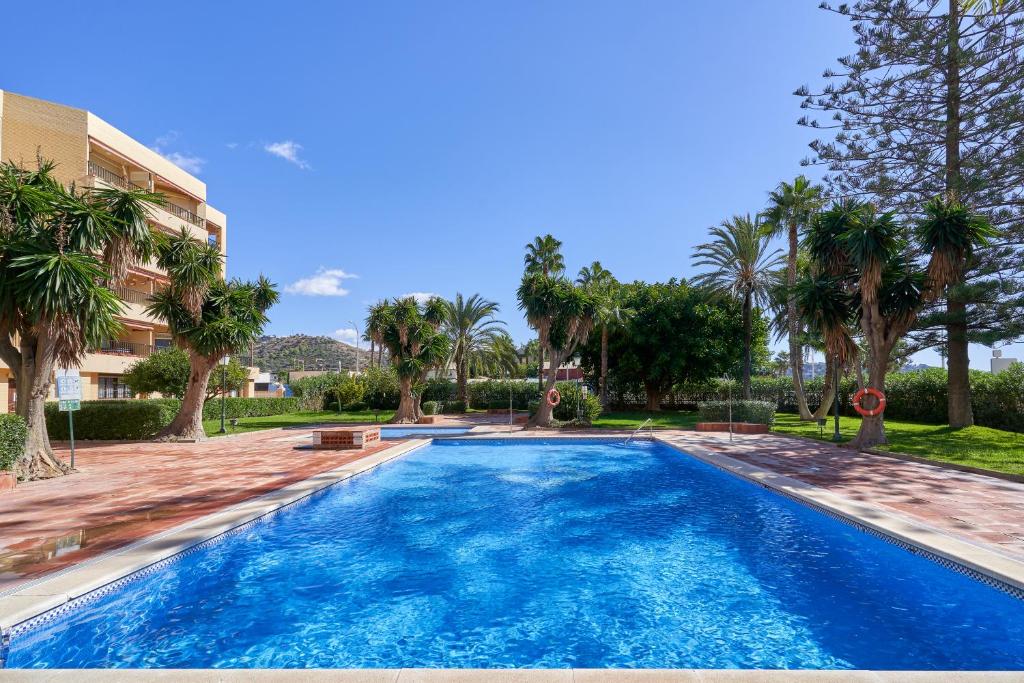 a swimming pool with palm trees and a building at Rosa Náutica La Herradura in Almuñécar