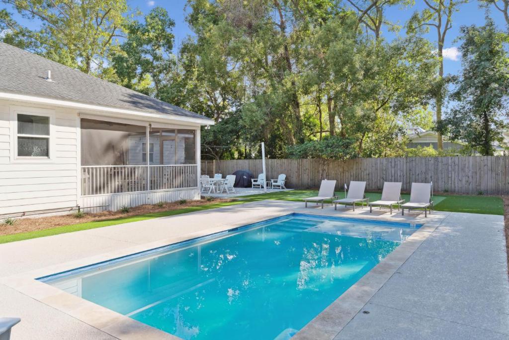 a swimming pool with chairs and a house at Getaway Cottage - 615 Bartow St in Saint Simons Island