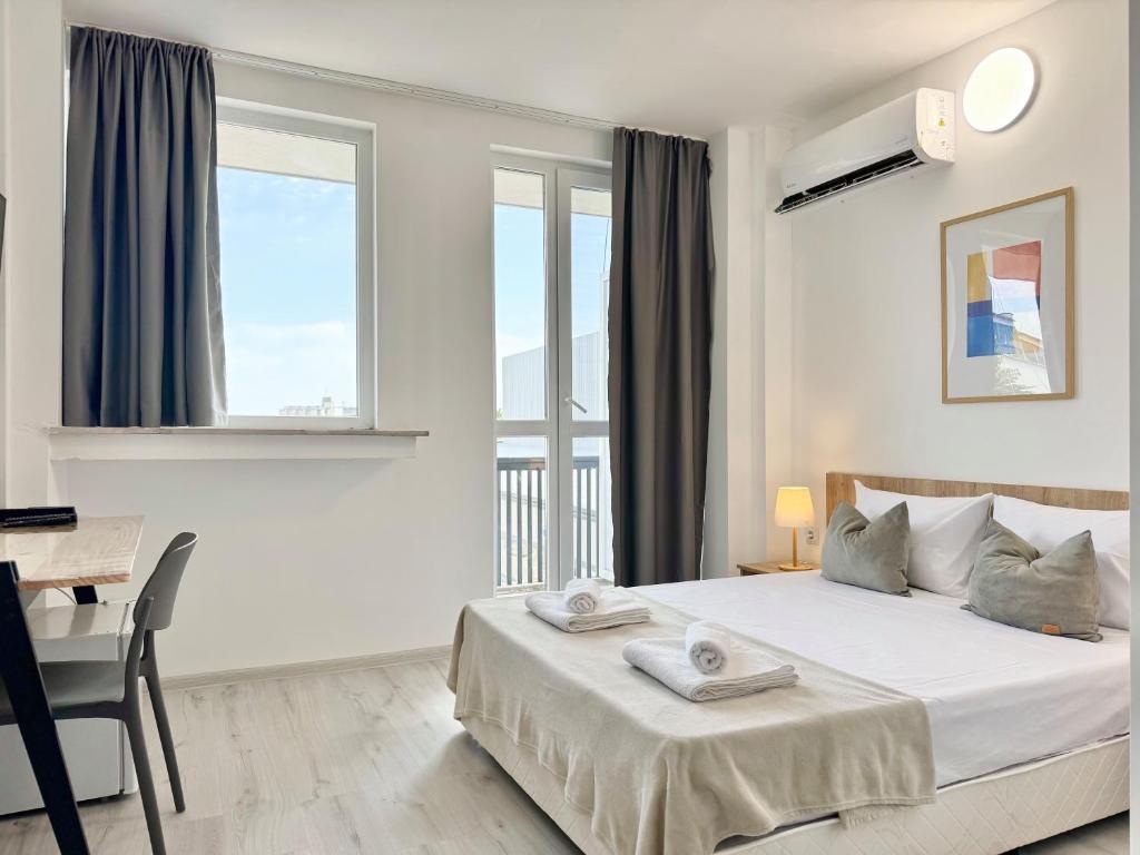 a white bedroom with a bed and a desk and windows at Студия за нощувки - Стара Загора in Stara Zagora