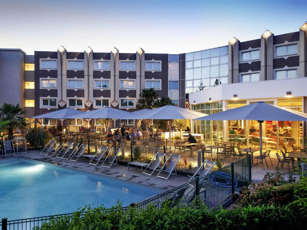 un hôtel avec une piscine, des tables, des chaises et des parasols dans l'établissement Novotel Clermont-Ferrand, à Clermont-Ferrand