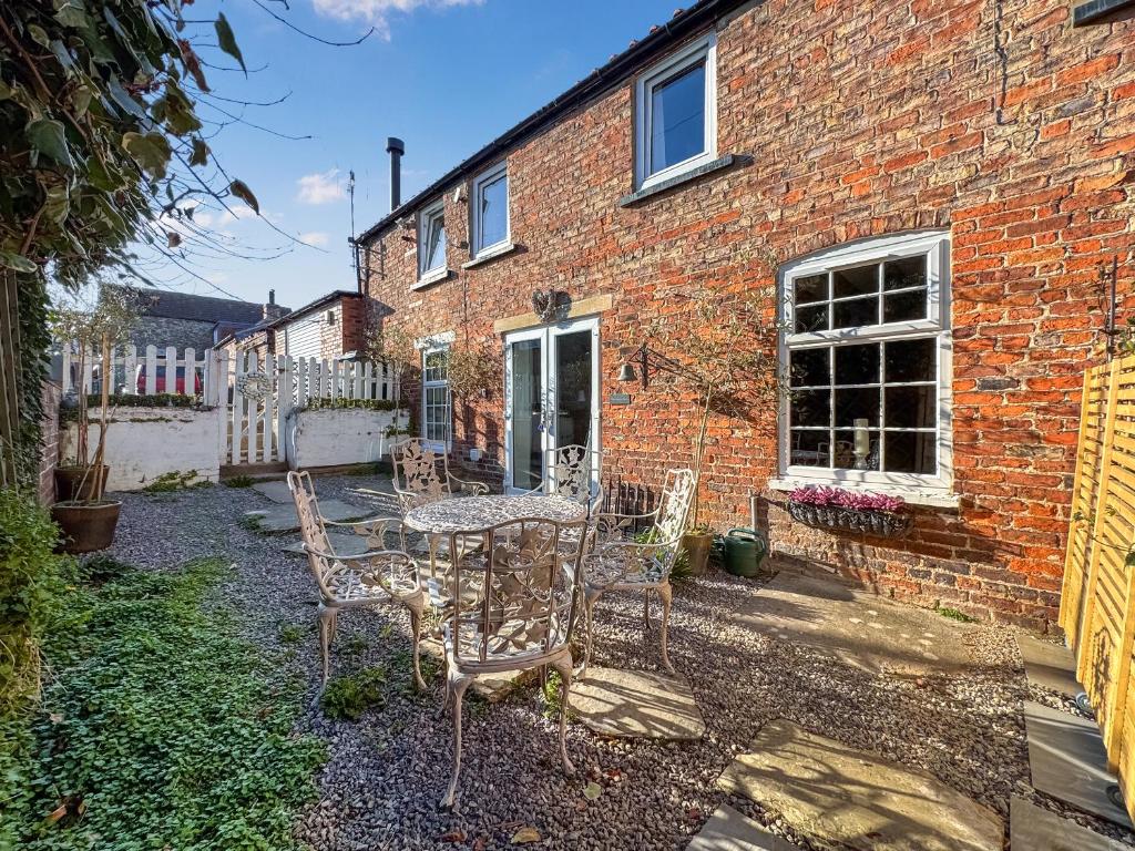 a patio with a table and chairs in front of a brick building at Warrington Mews-Uk48821 in Thornton Dale
