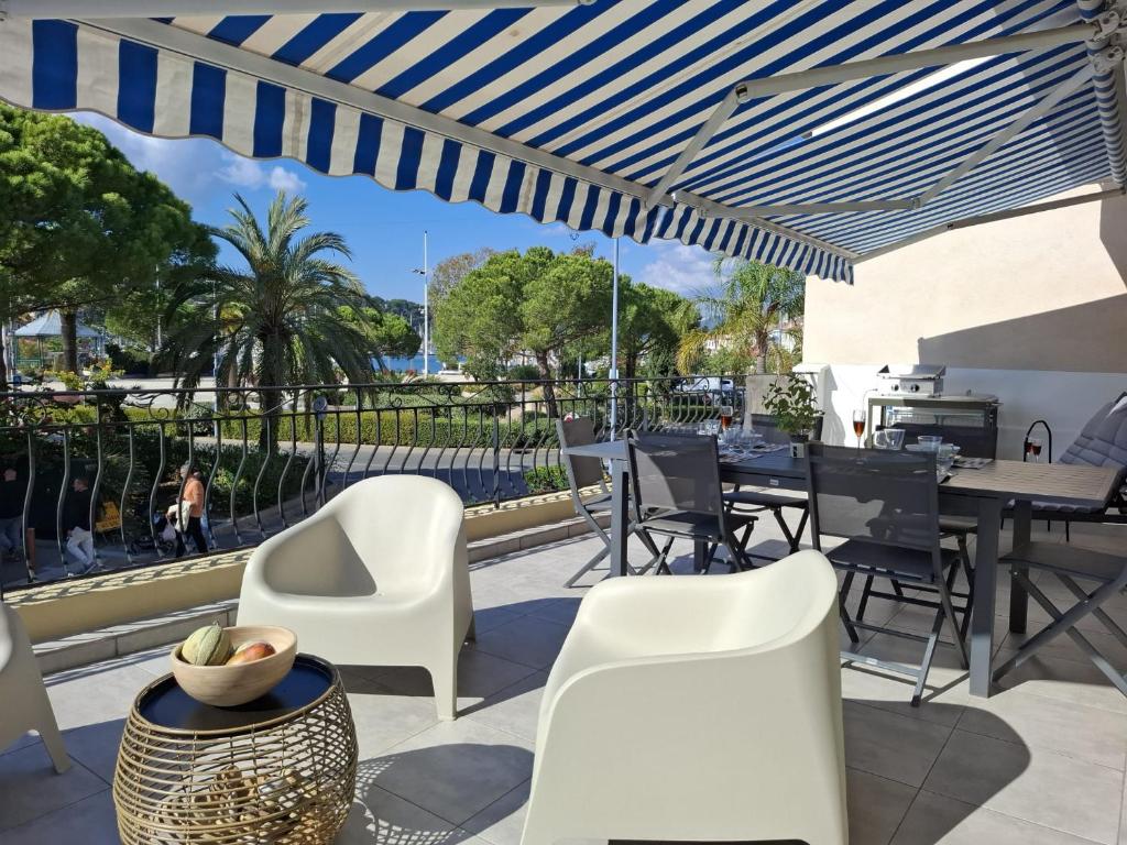 Un patio con sillas y mesas blancas y una sombrilla azul en Anatole - T3 - Moderne - Climatisé - 1er étage - Très grande terrasse 35 M2 - Vue magnifique et dégagée, en Saint-Mandrier-sur-Mer