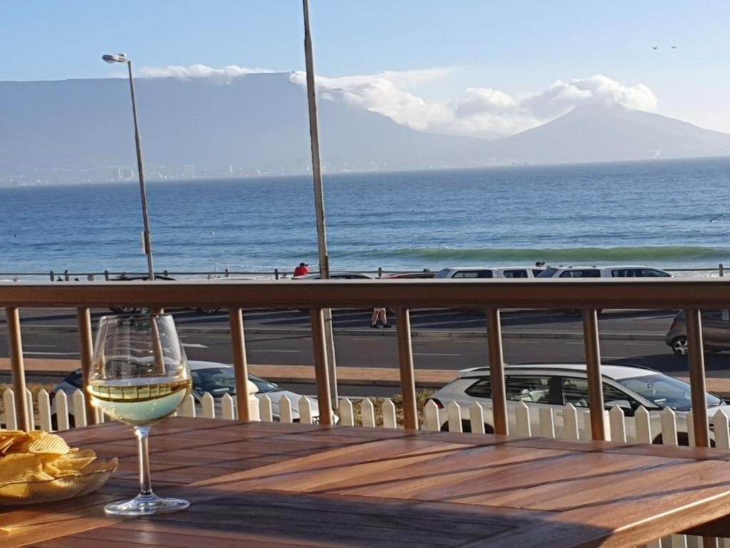 a glass of wine sitting on a table with the ocean at Bloubergstrand Beachfront Apartment Witsand 101 Tablemountain and ocean views in Cape Town