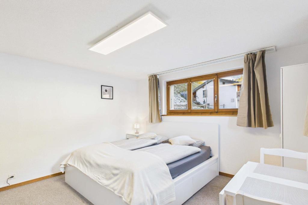 a white bedroom with a bed and a window at Comfortable studio near Saas-Fee ideal for couples in Saas-Grund