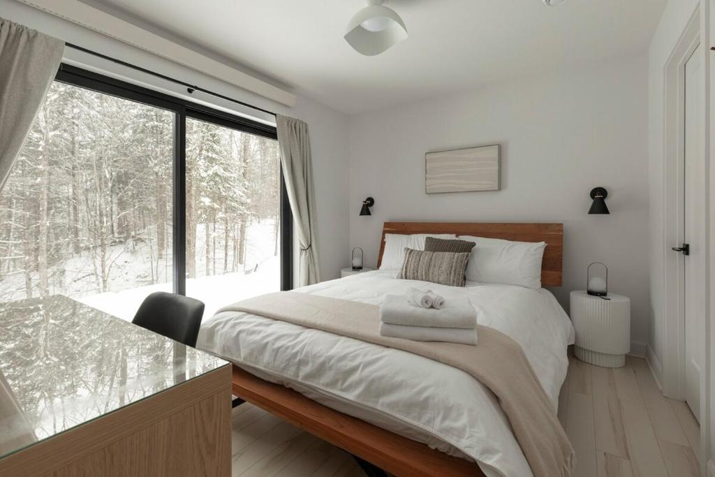ein Schlafzimmer mit einem Bett und einem großen Fenster in der Unterkunft Forest Refuge - Fire - HotTub - Tremblant 15 min in La Conception