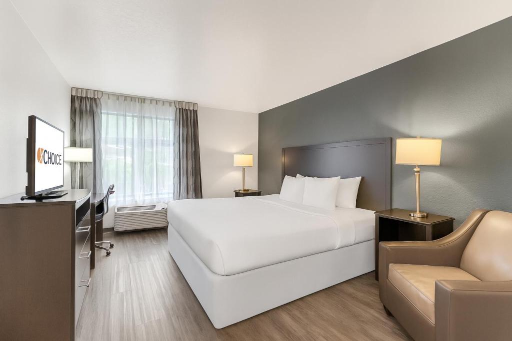 a hotel room with a large white bed and a chair at Clarion Inn Salt Lake City Airport in Salt Lake City