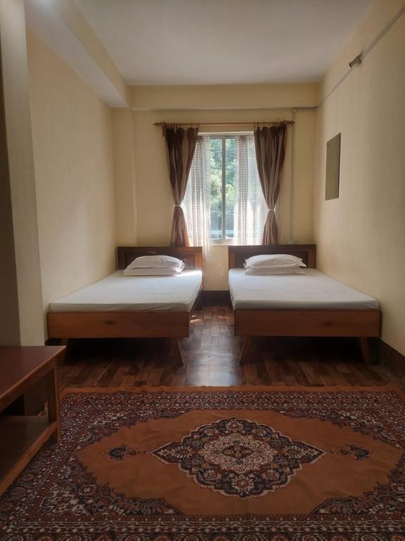 2 Betten in einem Zimmer mit einem Fenster und einem Teppich in der Unterkunft Mala cottage in Kalimpong
