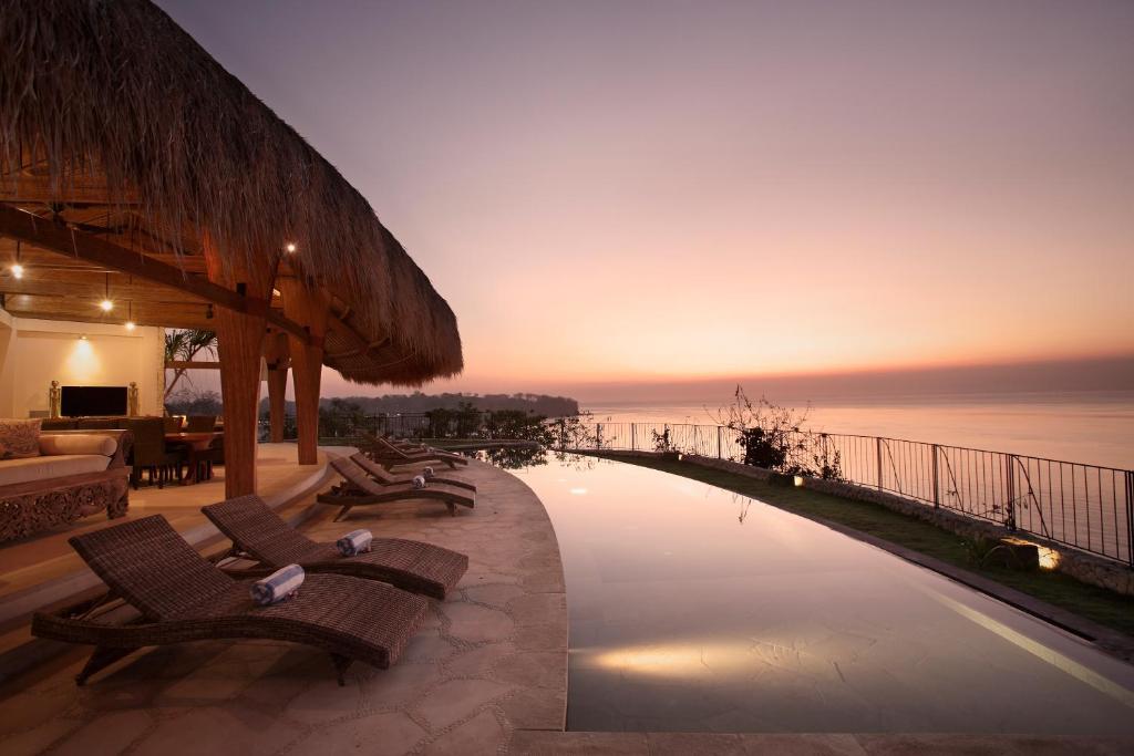 a resort pool with a view of the ocean at sunset at Villa Tanjung in Nusa Lembongan