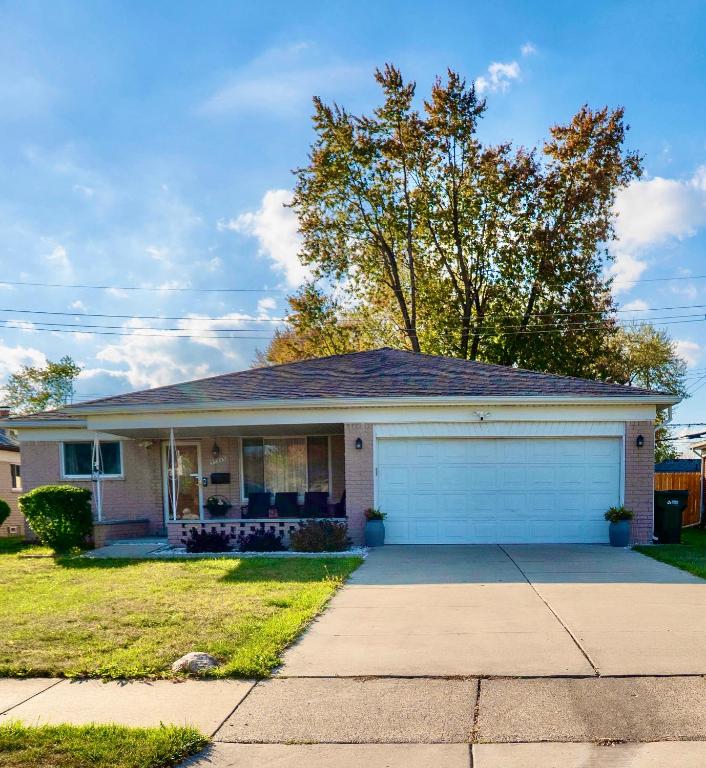 a white house with a garage in a yard at Charming Getaway Make Memories in Sterling Heights
