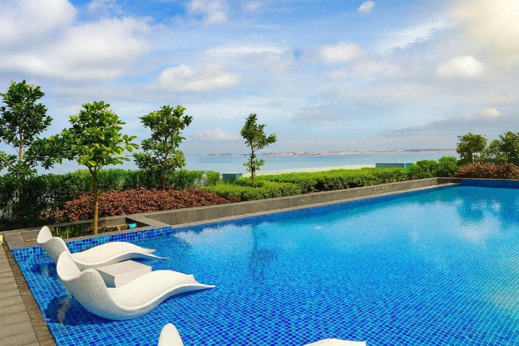 a swimming pool with two white chairs and the ocean at Modern Seaview 1BR Near Okada Manila Bay Airport 17 in Manila