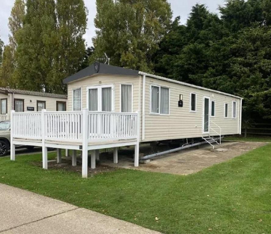 una casa móvil con porche y valla blanca en Caravan With Front Decking At Coopers Beach Holiday Park Ref 49080Pa, en East Mersea