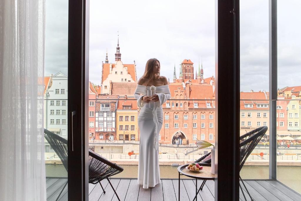 a woman in a white dress standing in front of a window at DEO PLAZA Apartments & Riverside by Downtown Apartments in Gdańsk