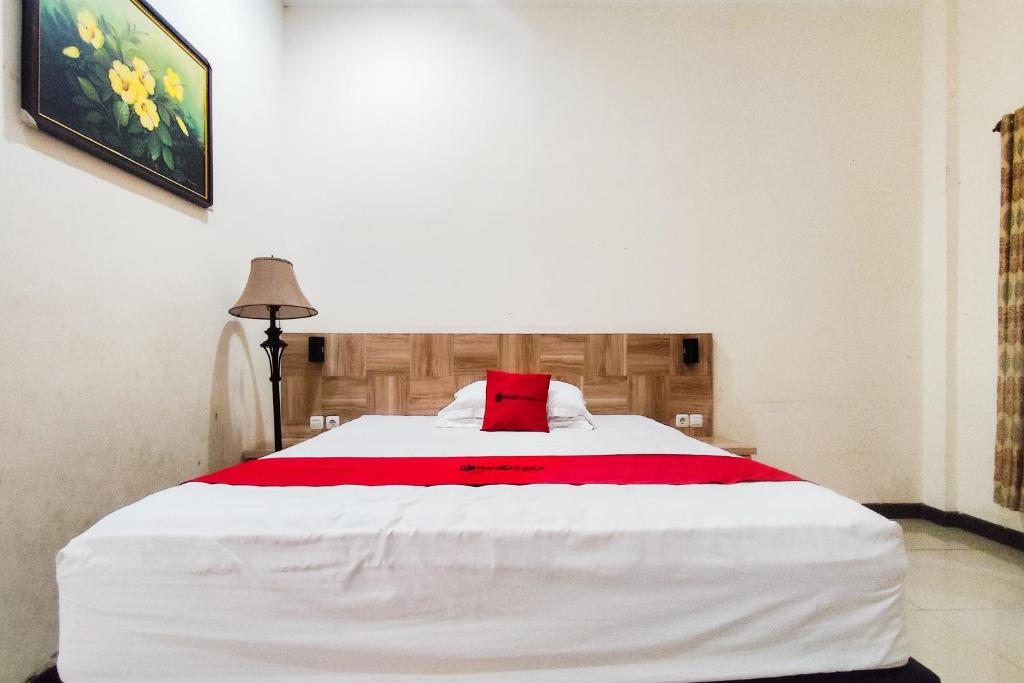 een slaapkamer met een groot wit bed met een rood kussen bij RedDoorz near Tugu Bandara Sulthan Thaha Jambi in Sultan Thaha Airport