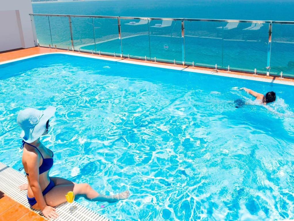 2 personnes nagent dans une piscine dans l'établissement Paris Luxury Hotel & Apartment Nha Trang, à Nha Trang