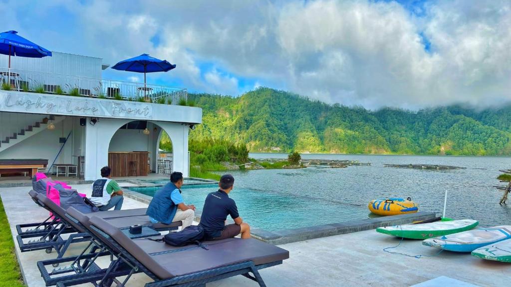 three men sitting on a table next to a body of water at Lushy Hostel Kintamani in Kubupenlokan