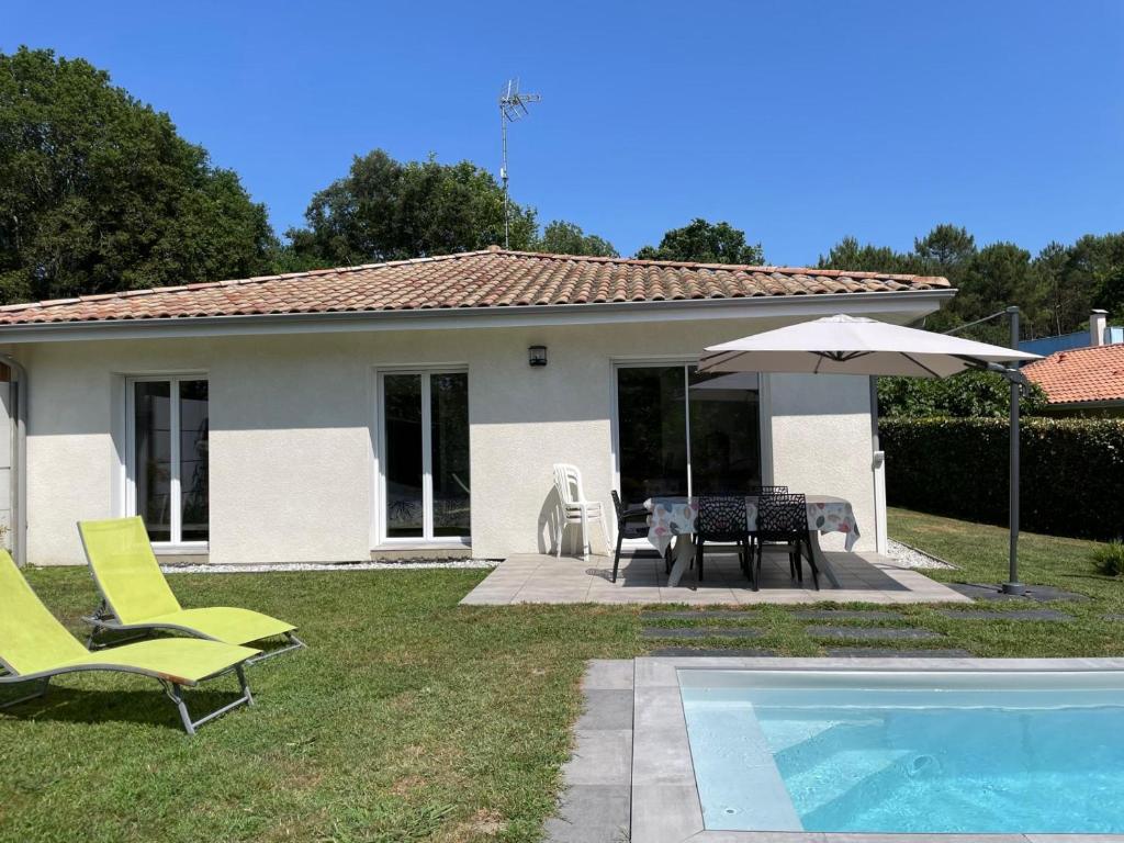 a house with a pool and chairs and an umbrella at Maison Solyselva Piscine- Proche océan- Climatisée in Saubion