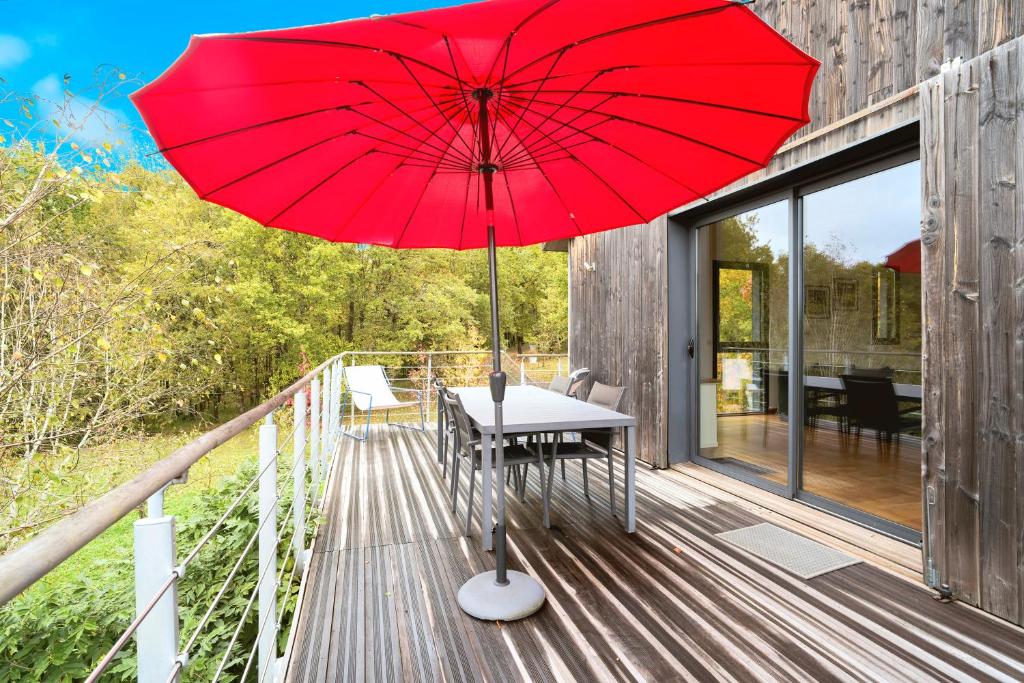 une table avec un parasol rouge sur une terrasse dans l'établissement Loft Ôvebas - Domaine De L 'ô, à Bellacaud