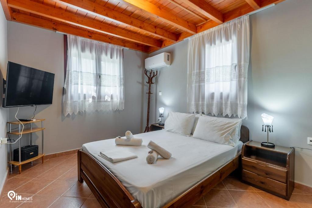 a bedroom with a bed with white sheets and a tv at Myrsini's House - Neapoli Garden & Grove Retreat 