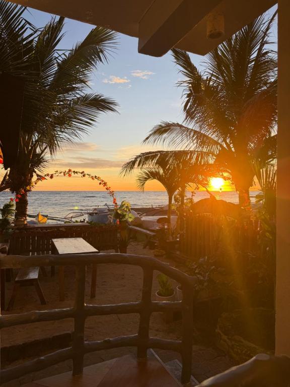 a sunset on the beach with a table and palm trees at Kobe's Beachfront Haven in Siquijor