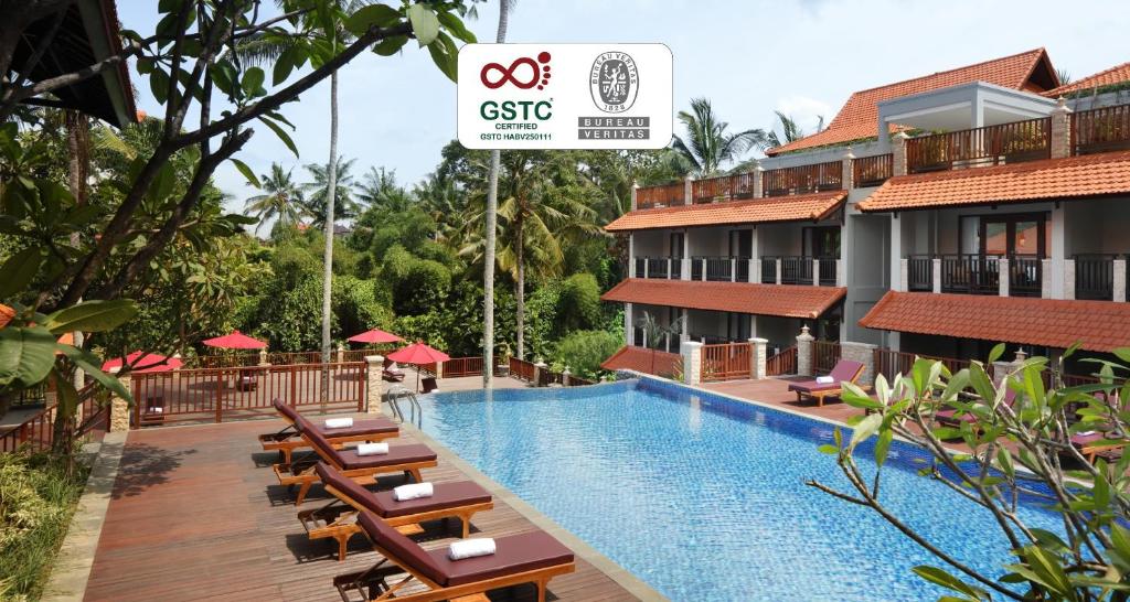 Un complejo turístico con piscina y mesas y sillas de madera. en Best Western Premier Agung Resort Ubud, en Ubud