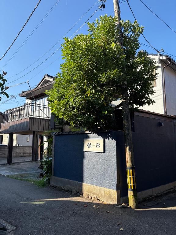 a tree in front of a building with a fence at Minshuku Ginmatsu in Kanazawa