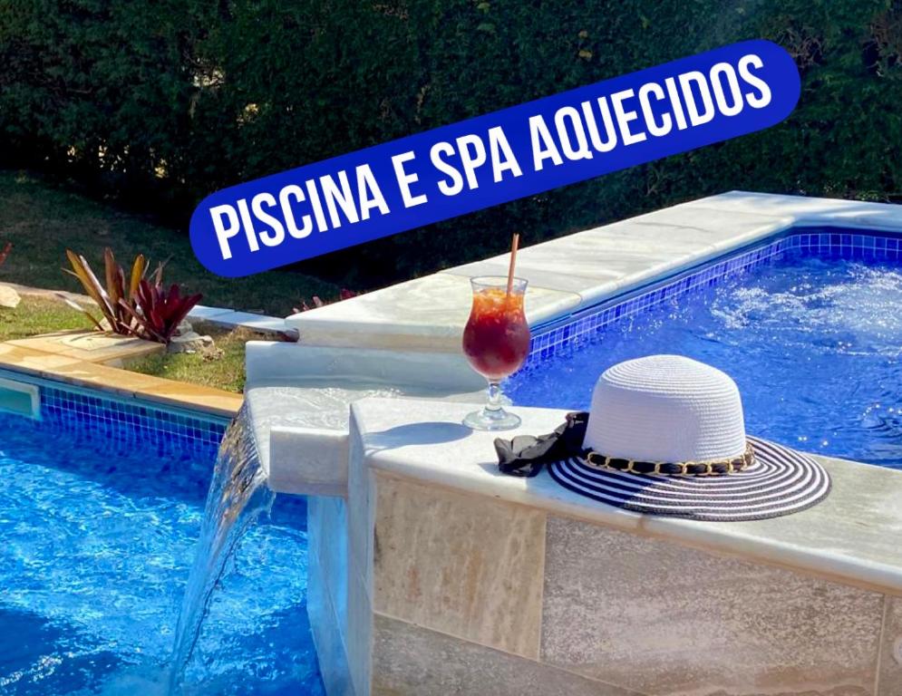 une boisson et un chapeau posés sur une table près d'une piscine dans l'établissement CHACARA THA&THI COND FECHADO WI FI SPA e PISC AQUECECIMENTO SOLAR, à Bom Jesus dos Perdões