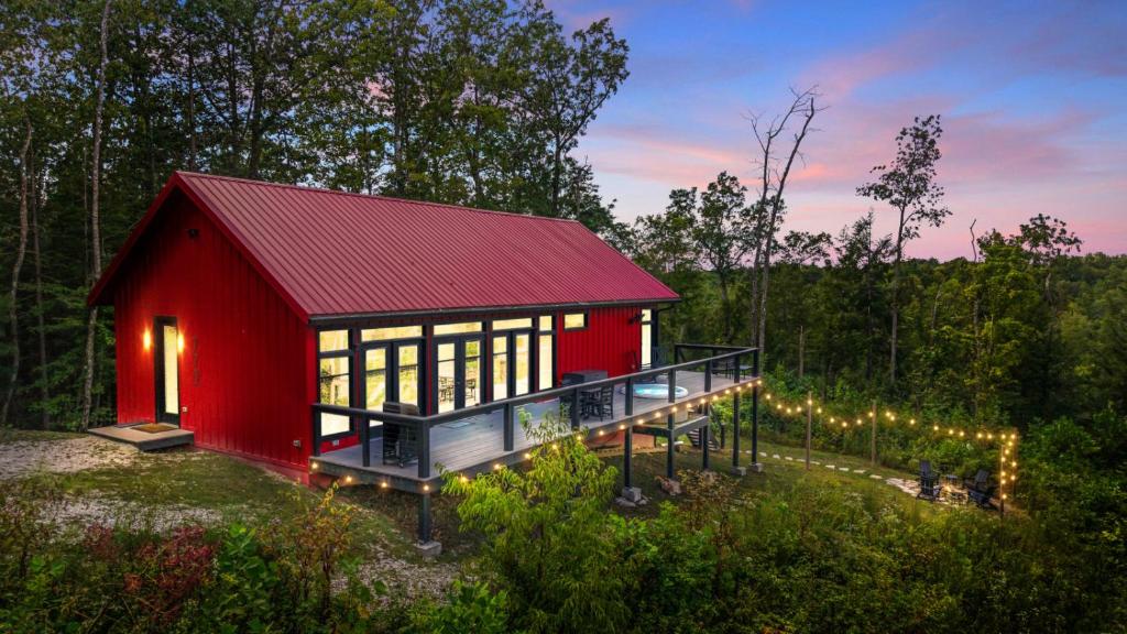 eine rote Hütte mit rotem Dach im Wald in der Unterkunft Luxury Hot-Tub WiFi - A Red River Barnhouse in Campton