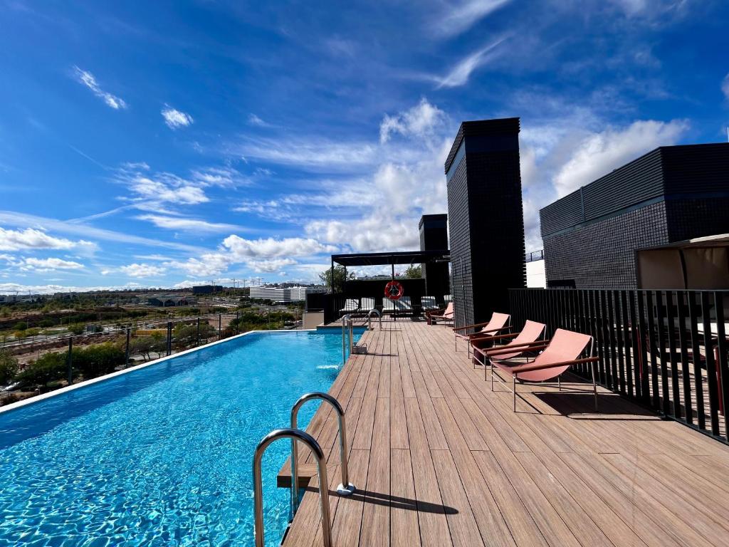 a deck with chairs and a swimming pool on a building at Calido Valdebebas in Madrid