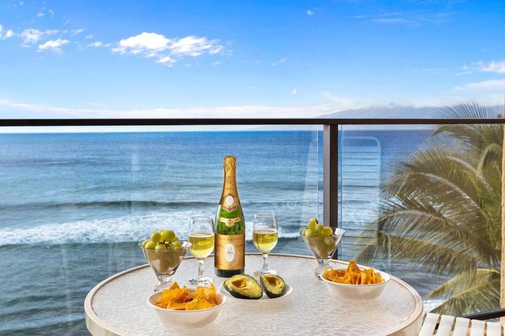 a table with a bottle of wine and bowls of food at Mahana 713 · MA 713 Luxury OceanFront Studio in Kahana