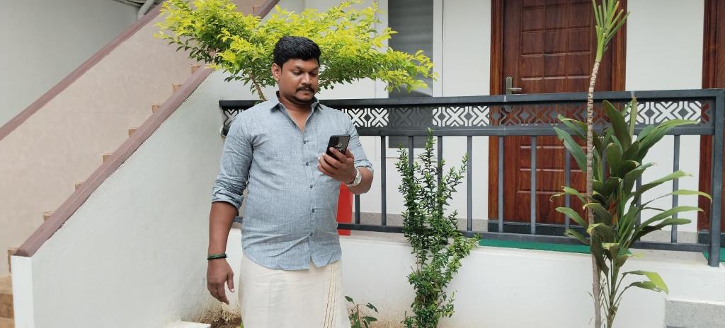 a man standing in front of a building looking at his cell phone at SMK homestay in Rāmeswaram