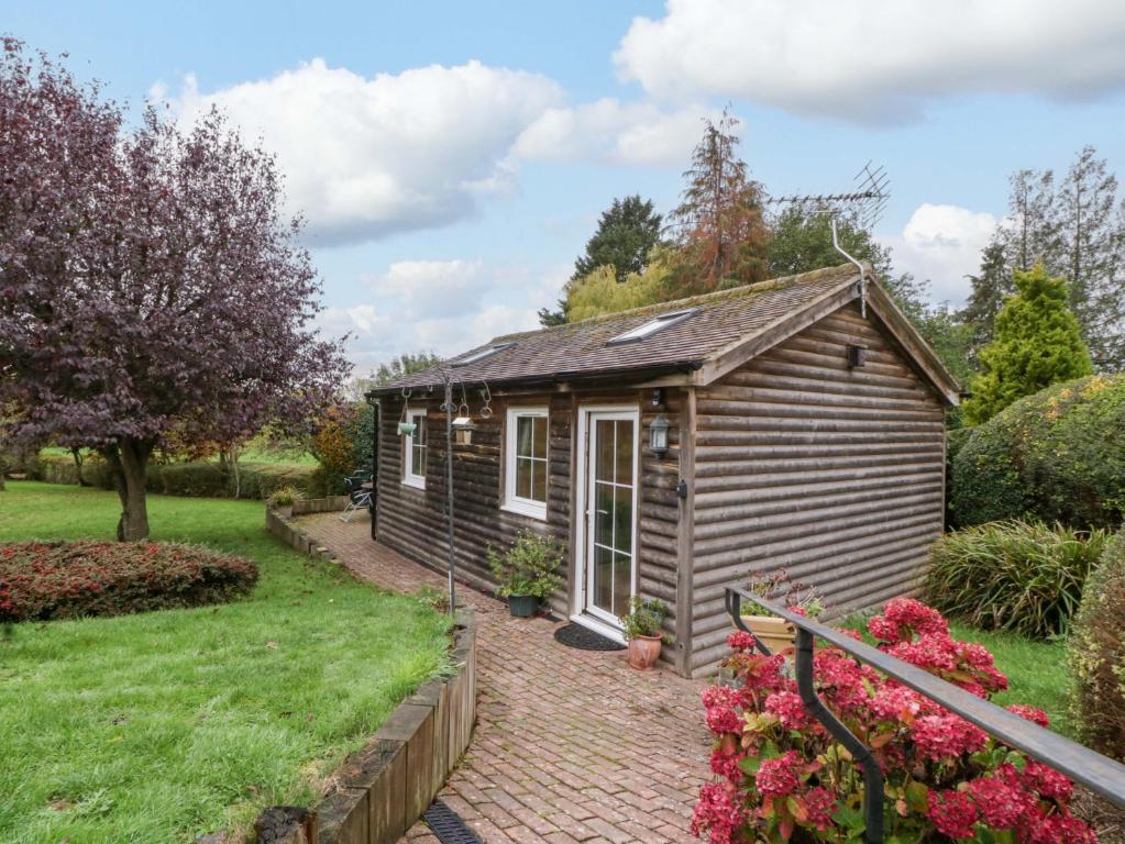 a small shed in a garden with a brick driveway at The Log Cabin in Gloucester