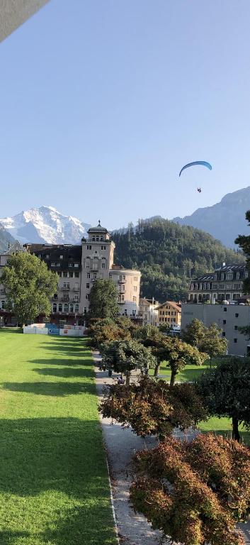 a paraglider flying over a park with trees and buildings at SAVOY 26 in Interlaken