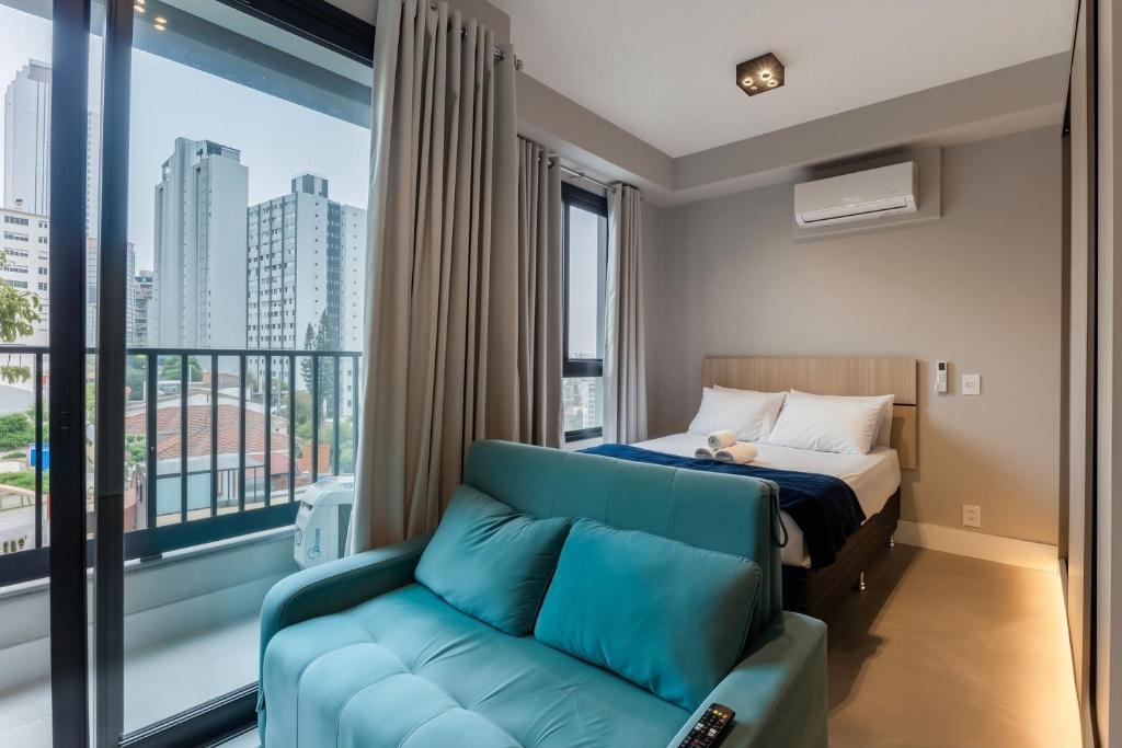 a bedroom with a bed and a couch in front of a window at Studios Vila Madalena com Ar condicionado | Delfhy in Sao Paulo