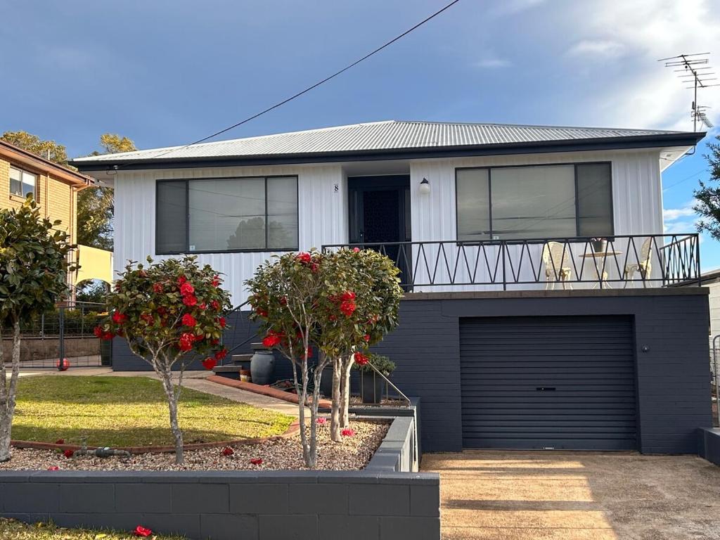 a white house with a garage and two trees at Gravity Stayz in Batehaven