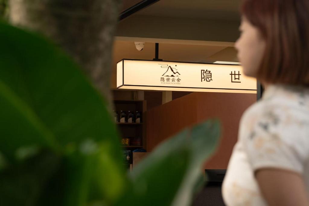 Eine Frau steht in einem Raum mit einem Schild in der Unterkunft Yinshi Yunshe Private Hot Spring Villa in Dujiangyan in Dujiangyan