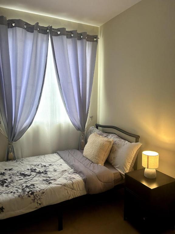 a bedroom with a bed with blue curtains and a window at 2-bedroom unit with Sea & Mountain View in Dumaguete