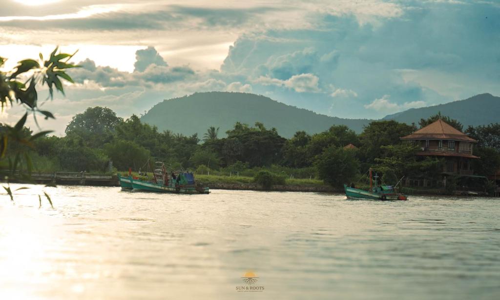 two boats on the water in front of a building at Sun Hostel and Restaurant Kampot in Kampot