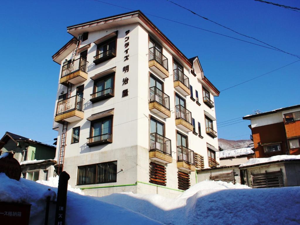 een hoog wit gebouw met sneeuw ervoor bij Sunrise Meiji-ya in Nozawa Onsen