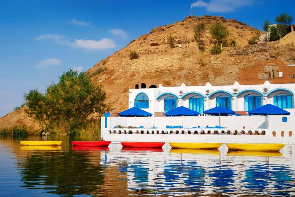 a boat with umbrellas on the water in front of a building at Nubian Spirit in Aswân Reservoir Colony